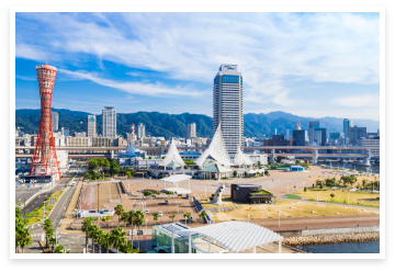 青空と山々を背景に高層ビルやタワーが立ち並ぶ神戸の風景